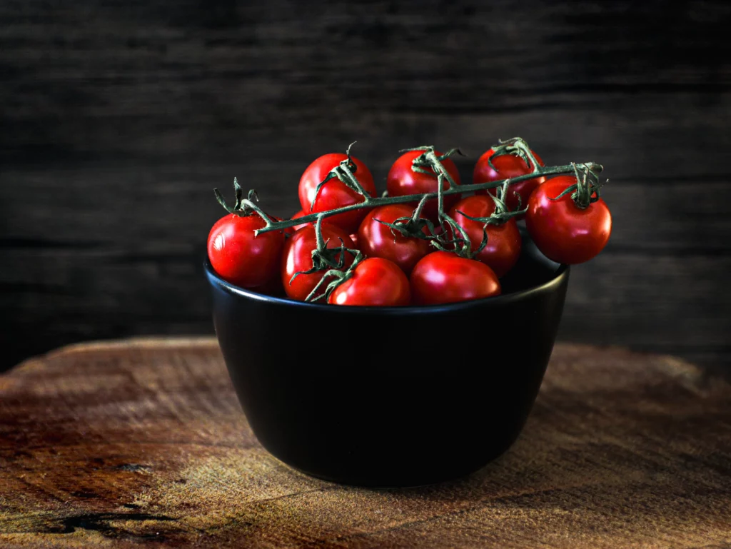 schwarze schale mit roten tomaten auf holzbrett von food fotograf hannover, dem fotograf in der nähe.