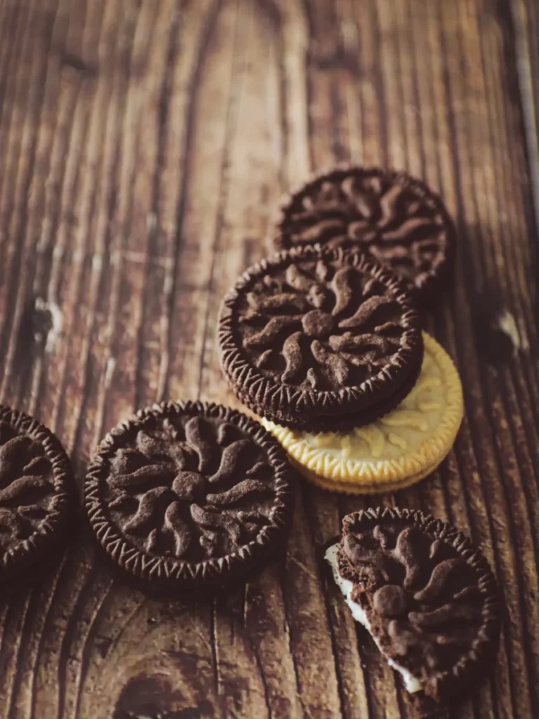 Stapel von Oreo-Keksen auf einer dunklen Holzoberfläche mit einem angebissenenem Keks unten rechts.