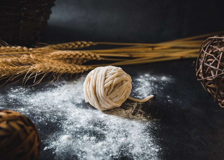 Der Food Fotograf - Eine Kugel aus rohem Nudelteig liegt auf einer bemehlten Oberfläche, im Hintergrund sind Weizenhalme und geflochtene Korbwaren zu sehen. Lecker Essen fotografieren.
