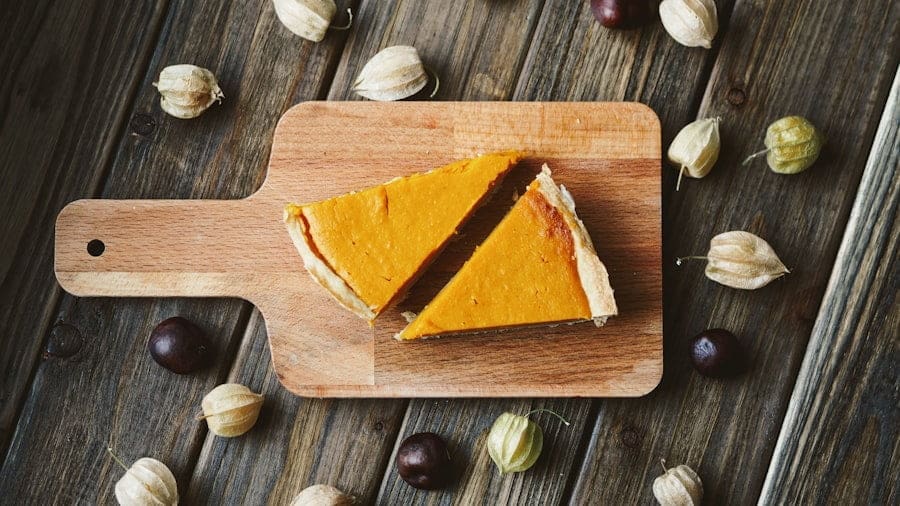 Food Fotograf Zwei Stücke Kürbiskuchen auf einem Holzschneidebrett, umgeben von Kapstachelbeeren und verstreuten dunklen Beeren auf einer rustikalen Holzoberfläche. Essen fotografieren