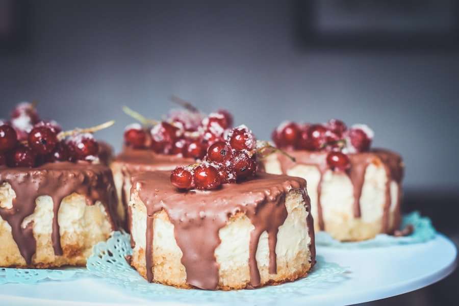 Der Food Fotograf - Drei quadratische Stücke Käsekuchen, überzogen mit einer dicken, tropfenden Schicht Schokolade und garniert mit glasierten roten Johannisbeeren, werden auf einer weißen Platte mit blauen Deckchen präsentiert. Der Hintergrund ist verschwommen und unscharf. Lecker Essen fotografieren.