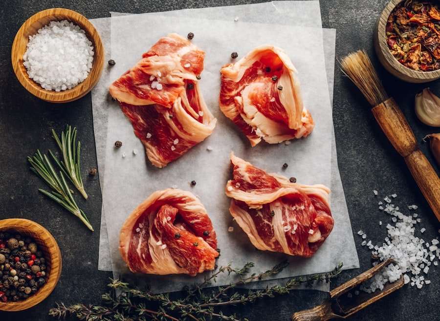 Food Fotograf Hannover - Vier Scheiben rohes Rindfleisch auf einem Blatt Backpapier liegen auf einer dunklen Oberfläche, perfekt für Food-Fotografie. Um sie herum stehen Schalen mit grobem Salz, ganzen Pfefferkörnern und getrockneten Kräutern. Frischer Rosmarin, eine Knoblauchknolle und ein Backpinsel runden die kulinarische Hintergrundszene ab. Food Fotografie Hannover.