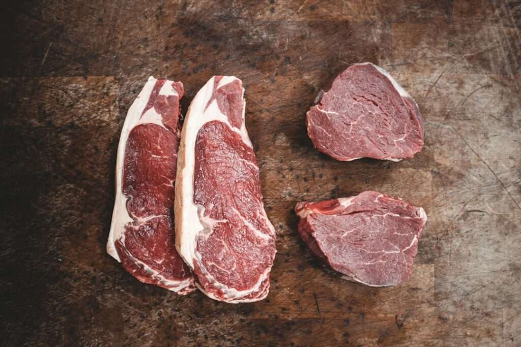Food Fotograf Hannover - Ein Holztisch mit zwei Stücken rohem Ribeye-Steak links und zwei Stücken rohem Filet-Mignon-Steak rechts, perfekt als Hintergrund für Food-Fotografie. Die Oberfläche des Tisches weist einige Gebrauchsspuren auf. Food Fotografie Hannover.