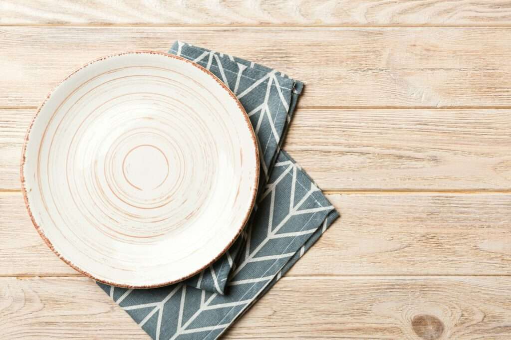 Top view on colored background empty round white plate on tablecloth for food.